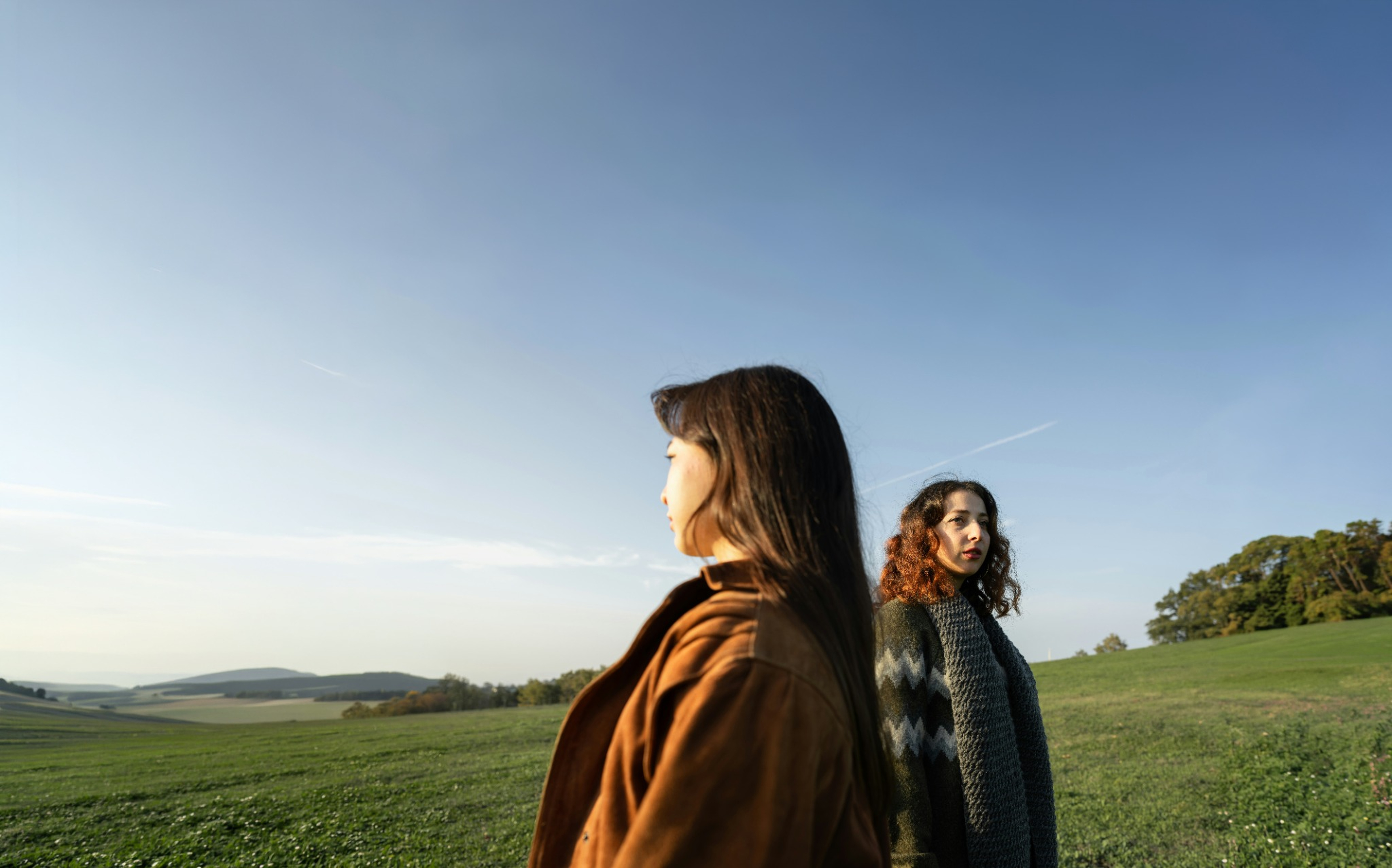 Two women standing in a green field under a wide blue sky